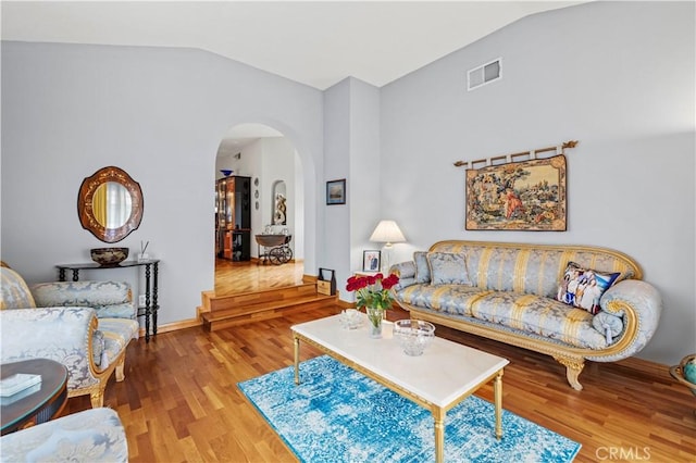 living room with arched walkways, vaulted ceiling, baseboards, visible vents, and wood finished floors