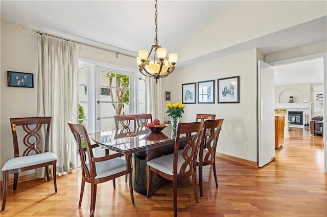 dining space featuring vaulted ceiling, baseboards, a chandelier, a glass covered fireplace, and light wood-style flooring