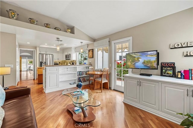 living area featuring arched walkways, vaulted ceiling, and light wood finished floors