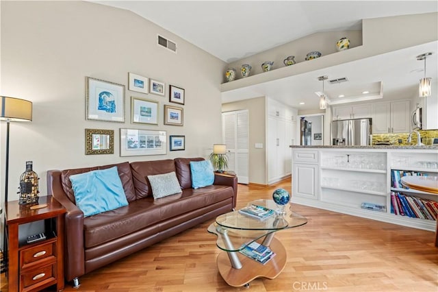 living room with vaulted ceiling, light wood-style floors, and visible vents