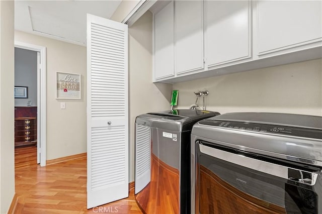 laundry area with light wood-type flooring, baseboards, independent washer and dryer, and cabinet space