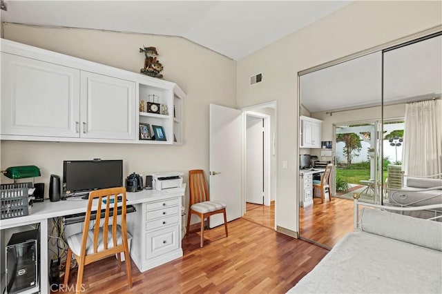 home office with visible vents, vaulted ceiling, built in study area, and light wood-style flooring