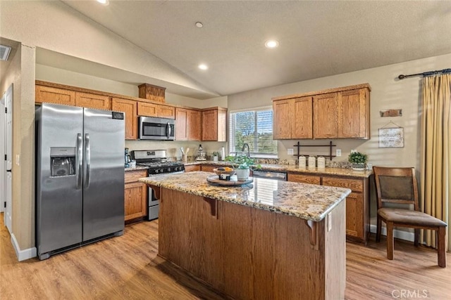 kitchen with appliances with stainless steel finishes, light wood-style floors, brown cabinets, a kitchen island, and lofted ceiling