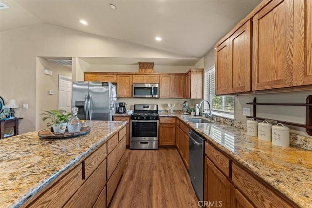 kitchen featuring dark wood-type flooring, appliances with stainless steel finishes, a sink, lofted ceiling, and brown cabinets