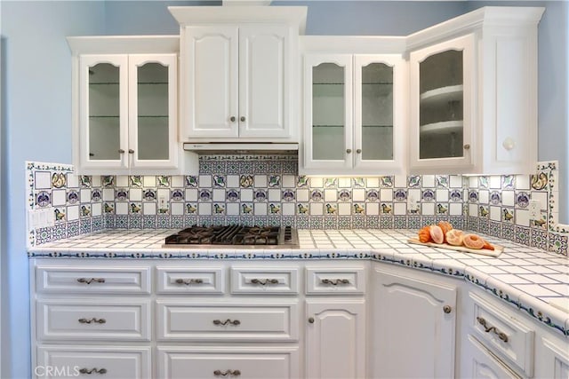 kitchen with backsplash, white cabinets, glass insert cabinets, and stainless steel gas cooktop