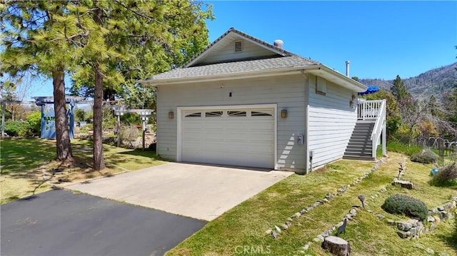 view of side of home with stairs, a shingled roof, a mountain view, and a detached garage
