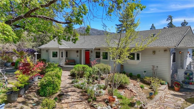 ranch-style home with a mountain view, a shingled roof, and covered porch