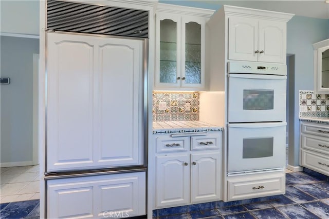 kitchen with white double oven, glass insert cabinets, white cabinetry, decorative backsplash, and baseboards