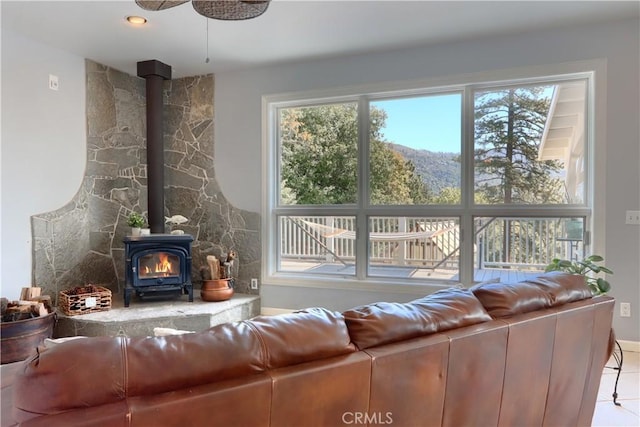 living room with tile patterned floors, a wood stove, and a ceiling fan