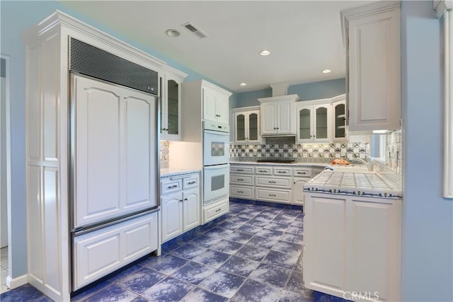 kitchen with glass insert cabinets, double oven, white cabinetry, visible vents, and decorative backsplash
