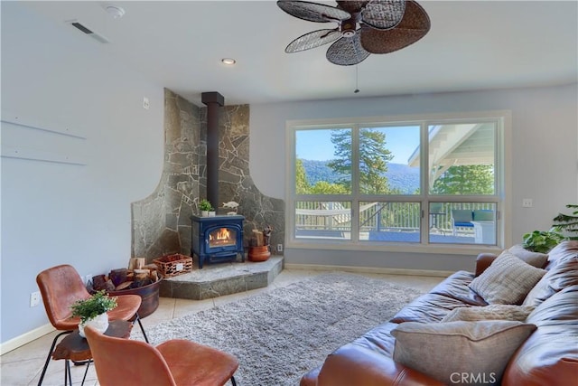 tiled living room featuring a healthy amount of sunlight, a wood stove, baseboards, and a ceiling fan