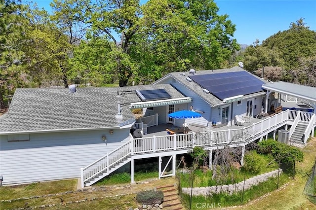 rear view of house with stairs, solar panels, a wooden deck, and a shingled roof