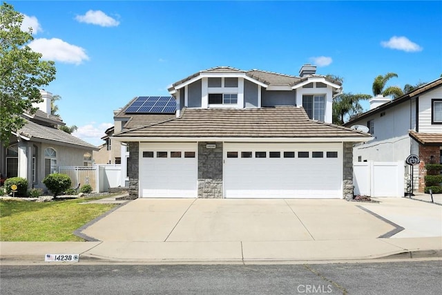 traditional-style house with concrete driveway, solar panels, a tiled roof, and fence