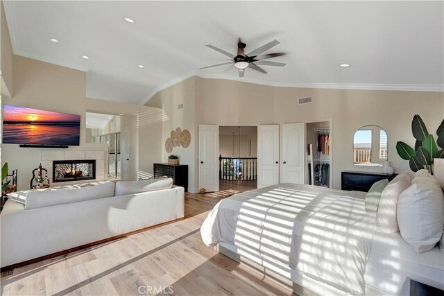 bedroom with visible vents, ornamental molding, a walk in closet, wood finished floors, and a tile fireplace
