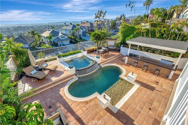 view of swimming pool featuring exterior kitchen, a residential view, a patio, a fenced backyard, and a pool with connected hot tub