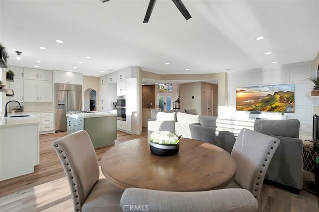 dining space with light wood finished floors, arched walkways, recessed lighting, and a ceiling fan