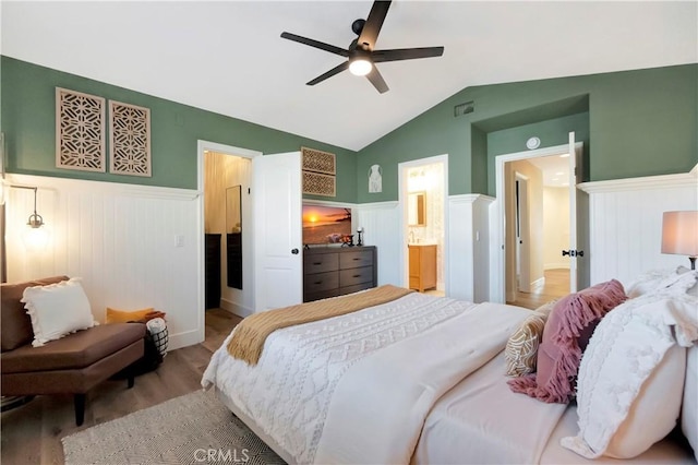 bedroom with ensuite bath, a wainscoted wall, visible vents, lofted ceiling, and wood finished floors