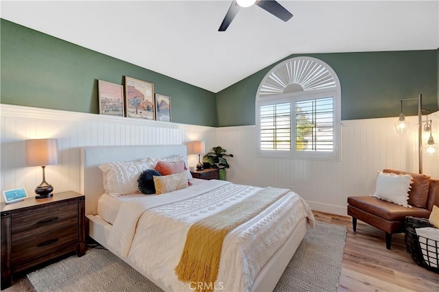bedroom featuring a ceiling fan, wood finished floors, wainscoting, and vaulted ceiling