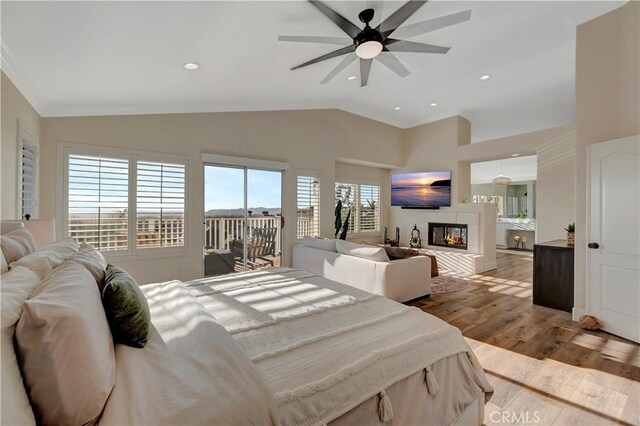bedroom with access to outside, crown molding, vaulted ceiling, wood finished floors, and a tiled fireplace
