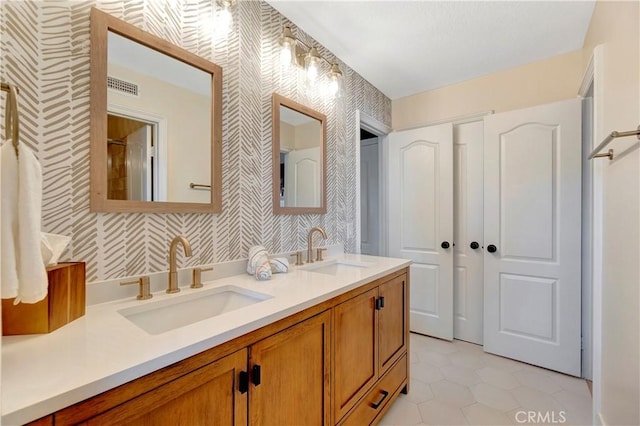 bathroom with a sink, visible vents, double vanity, and wallpapered walls