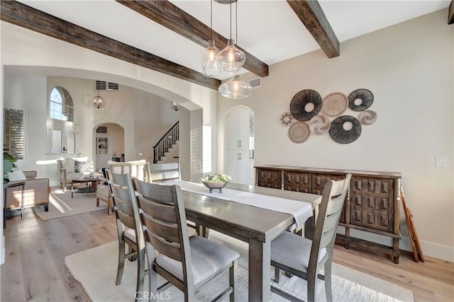 dining area with a wealth of natural light, arched walkways, stairway, and light wood-style floors