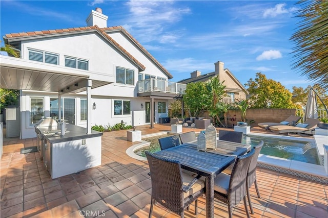 back of house with an outdoor kitchen, outdoor lounge area, stucco siding, a balcony, and a chimney