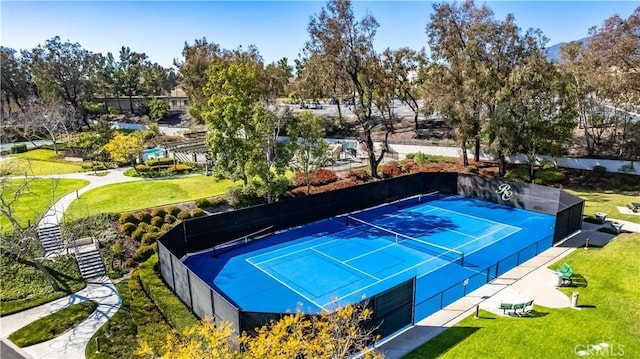 view of tennis court featuring fence and a lawn