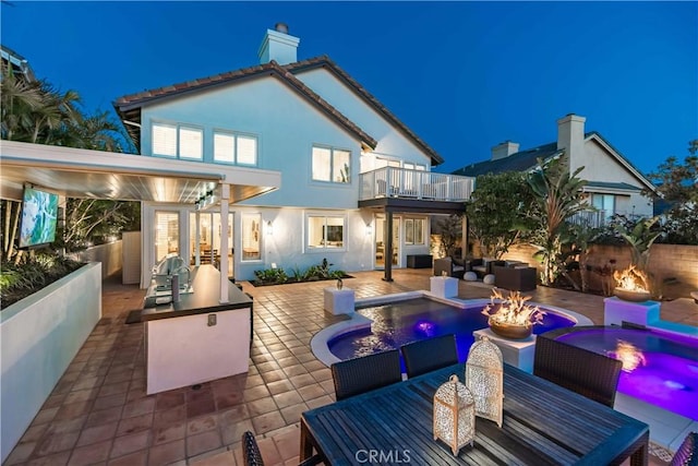 back of house at twilight featuring area for grilling, a fenced backyard, stucco siding, a balcony, and outdoor dining area
