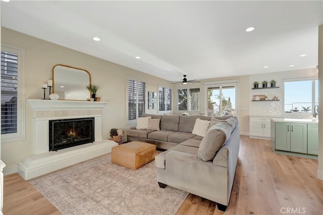 living area with light wood-style floors, a healthy amount of sunlight, a ceiling fan, and a warm lit fireplace