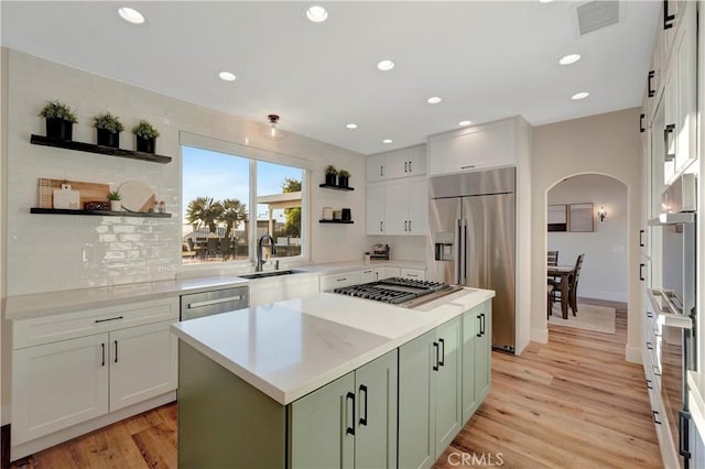 kitchen featuring green cabinets, open shelves, appliances with stainless steel finishes, arched walkways, and a sink