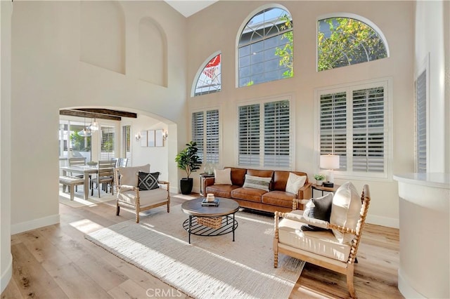 living area featuring arched walkways, wood finished floors, a towering ceiling, and baseboards