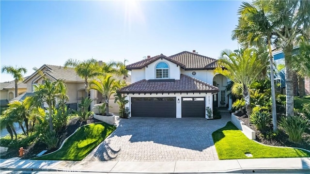 mediterranean / spanish-style home with a garage, stucco siding, decorative driveway, and a tile roof