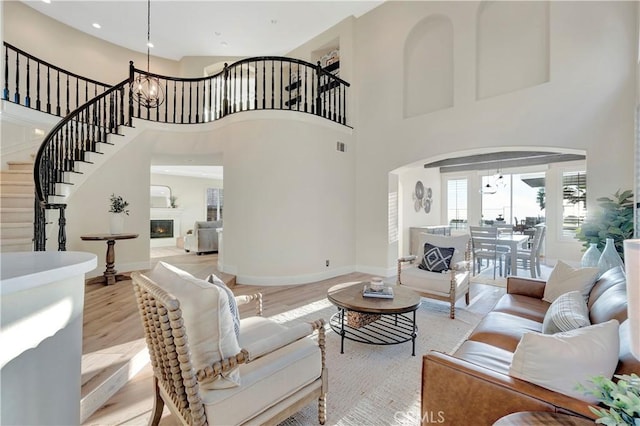 living area with light wood-style floors, arched walkways, a glass covered fireplace, stairway, and a high ceiling