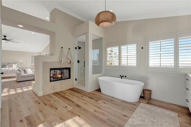 full bathroom with a multi sided fireplace, a freestanding tub, crown molding, a shower stall, and wood finished floors