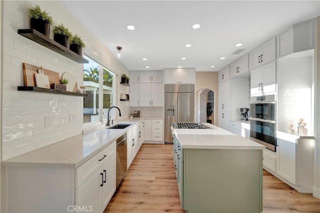 kitchen featuring a center island, open shelves, light wood-style floors, appliances with stainless steel finishes, and arched walkways