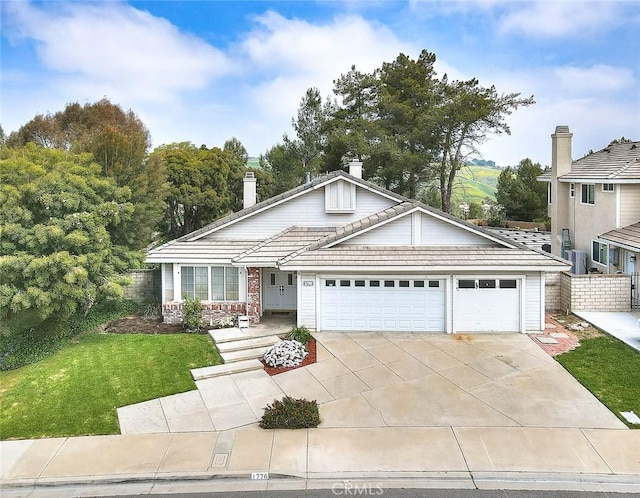 view of front facade featuring a chimney, driveway, a front yard, a garage, and a tiled roof