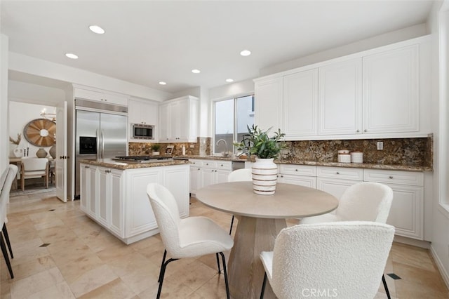 kitchen with built in appliances, white cabinetry, a kitchen island, decorative backsplash, and a sink