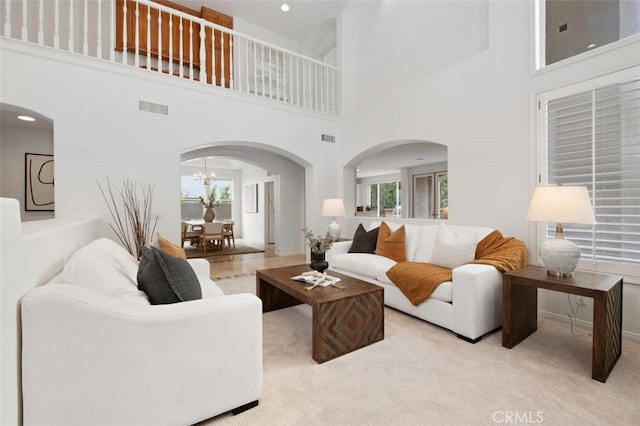 carpeted living area with arched walkways, a healthy amount of sunlight, and visible vents