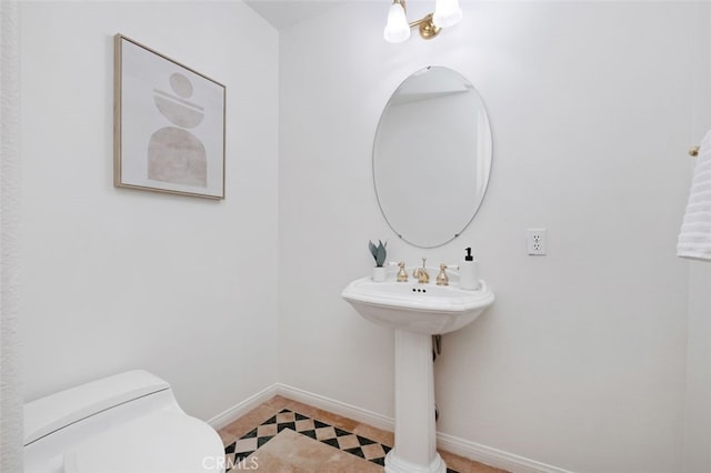 half bathroom with a sink, toilet, tile patterned flooring, and baseboards