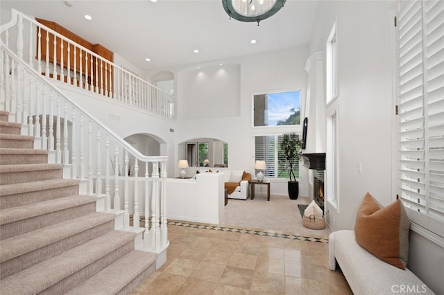 living area featuring a towering ceiling, recessed lighting, light carpet, stairs, and baseboards