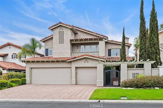 mediterranean / spanish house featuring a garage, stucco siding, decorative driveway, and a gate
