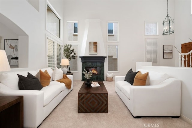 carpeted living area featuring a notable chandelier, a high ceiling, and a premium fireplace