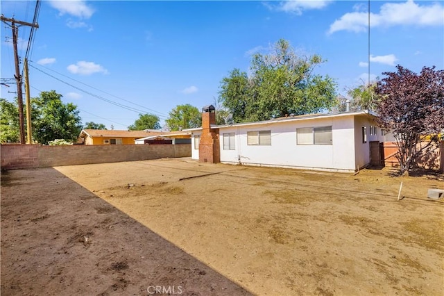 back of house featuring stucco siding, fence, and a chimney