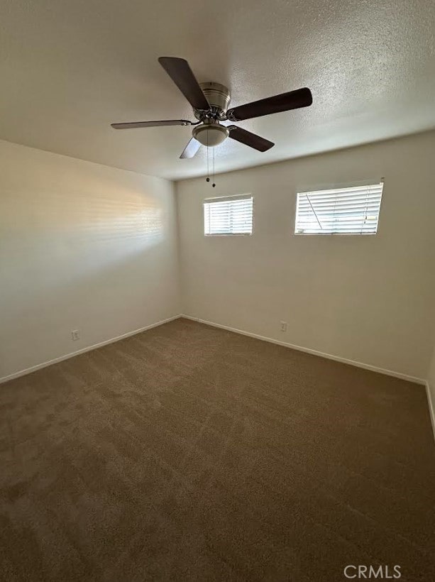 spare room with baseboards, dark carpet, and a ceiling fan