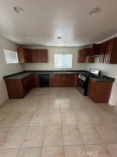 kitchen with light tile patterned floors, black dishwasher, dark countertops, stainless steel range with gas stovetop, and a sink