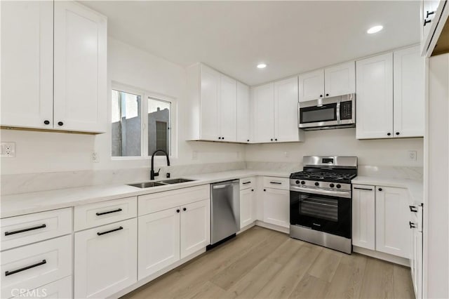 kitchen featuring recessed lighting, white cabinets, light wood-style floors, appliances with stainless steel finishes, and a sink