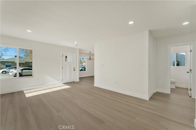 unfurnished living room with recessed lighting, a notable chandelier, light wood-style floors, and baseboards