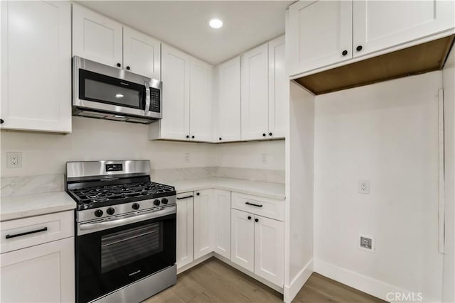 kitchen with stainless steel appliances, light stone countertops, light wood-style flooring, and white cabinets
