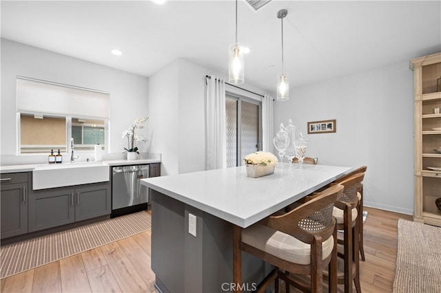 kitchen featuring light countertops, a sink, light wood-type flooring, a kitchen bar, and dishwasher