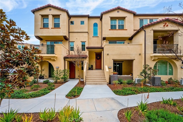view of front facade with stucco siding, central air condition unit, a tile roof, and a balcony